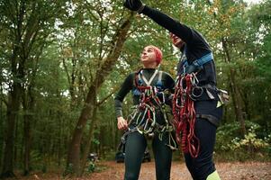 Male is showing something ,by ,hand and talking. Man and woman doing climbing in forest with use of safety equipment photo