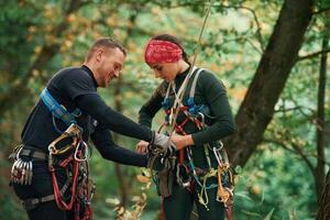 Man is helping the woman... Doing climbing in forest with use of safety equipment photo