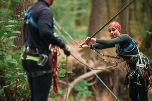 Preparing, the ropes. Ma,n and woman doing climbing in forest with use of safety equipment photo