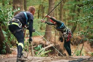 Preparing ,the, ropes. Man and, woman doing climbing in forest with use of safety equipment photo