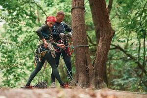 Setting up the ropes. Man and woman ,doing climbing in forest with use of safety equipment photo