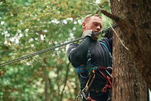 Process of preparing. Man, is, doing climbing in the forest by use of safety equipment photo