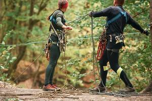 Preparing ,,the ropes. Man and woman doing climbing in forest with use of safety equipment photo