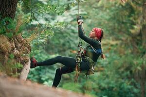 View from, the, side, hanging on ,the, rope. Woman is doing climbing in the forest by the use of safety equipment photo