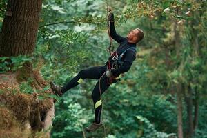 Hanging ,on, a rope. Man is doing climbing in the forest by use of safety equipment photo