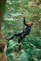Hanging, on a rope. Man is, doing climbing in the forest by use of safety equipment photo
