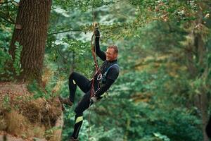 Up on the, rope, hanging,. Man is doing climbing in the forest by use of safety equipment photo