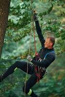 Side view, using the rope, hanging. Man is doing climbing in the forest by use of safety equipment photo