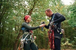 Standing together. Man and woman doing ,climbing in forest with use of safety equipment photo