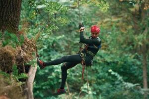 View, from, the side, hanging on the rope. Woman is doing climbing in the forest by the use of safety equipment photo