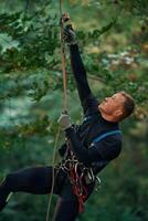 Man is doing climbing in the forest, by use of safety equipment photo