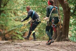 Setting up the ropes. Man and, woman doing climbing in forest with use of safety equipment photo