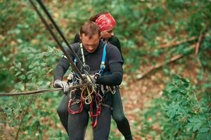 Going down. Man ,and,woman doing climbing in forest with use of safety equipment photo