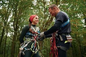 Standing, together. Man, and ,woman doing climbing in forest with use of safety equipment photo