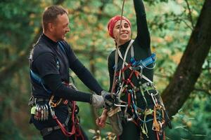 Man is helping the woman. Doing, climbing, in forest with use of safety equipment photo