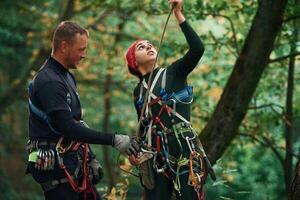 Man is helping, the, woman. Doing climbing in forest with use of safety equipment photo