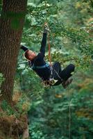 Side view, using the rope, hanging.. Man, is doing climbing in the forest by use of safety equipment photo
