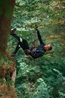 Hanging, on, a rope. Man is doing climbing in the forest by use of safety equipment photo