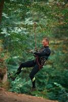Up on the,, rope, hanging. Man is doing climbing in the forest by use of safety equipment photo