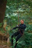 Activity, hanging on a ,rope. Man is doing climbing in the forest by use of safety equipment photo