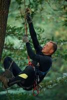 Side,, view, using the rope, hanging. Man is doing climbing in the forest by use of safety equipment photo