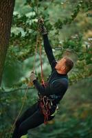 Side view, using the rope, hanging... Man is doing climbing in the forest by use of safety equipment photo