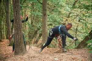 Standing on the ground and preparing. Man is doing climbing in the forest by use of safety equipment photo