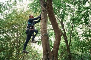 Extreme sports, high up. Man is doing climbing in the forest by use of safety equipment photo