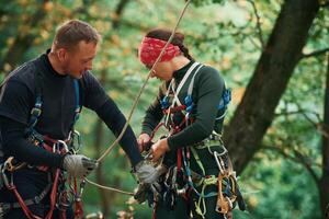 Man, is, helping the woman. Doing climbing in forest with use of safety equipment photo
