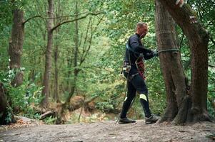 Standing, on, the ground and preparing. Man is doing climbing in the forest by use of safety equipment photo
