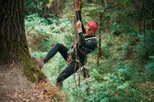 Focused,, on the climbing up. Woman is in the forest, using the safety equipment photo