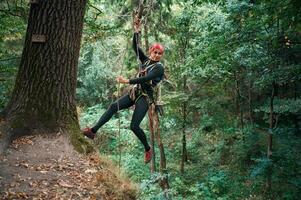 Looking, to the side, hanging on the rope. Woman is doing climbing in the forest by the use of safety equipment photo