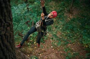 Focused on the, climbing up. Woman is in the forest, using the safety equipment photo