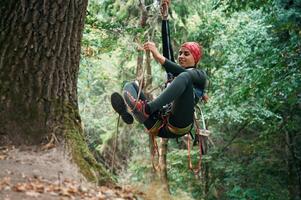 Focused on, the climbing, up. Woman is in the forest, using the safety equipment photo