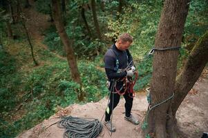 Standing on, the ground and preparing. Man is doing climbing in the forest by use of safety equipment photo