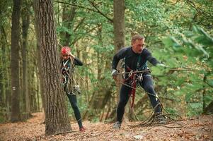 Standing,, together. Man and woman doing climbing in forest with use of safety equipment photo