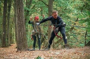 Standing together.. Man and woman, doing climbing in forest with use of safety equipment photo