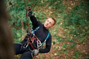On the, high tree, hanging. Man is doing climbing in the forest by use of safety equipment photo
