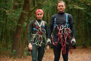 Standing, and posing. Man and woman doing climbing in forest with use of safety equipment photo