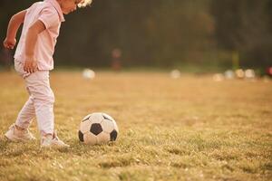 Soccer ball, is, on the ground. Cute little girl with curly hair is playing on the field at daytime photo