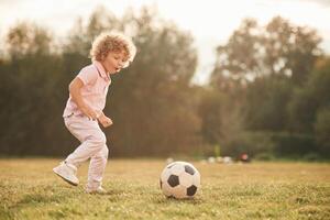 Soccer ball is on the ground.. Cute little girl with curly hair is playing on the field at daytime photo