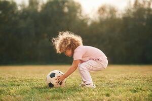 Soccer, ball ,is on the ground. Cute little girl with curly hair is playing on the field at daytime photo