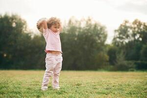 Holding, soccer ball in hands. Cute little girl with curly hair is playing on the field at daytime photo