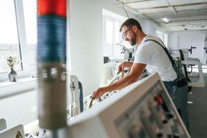 Standing by the machine. Handsome man is working at the factory of creating eco boxes photo