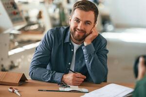 Posing, cheerful male. Handsome man, is ,working at the factory of creating eco boxes photo
