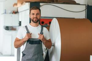 By, the rounded machine for making paper. Handsome man is working at the factory of creating eco boxes photo