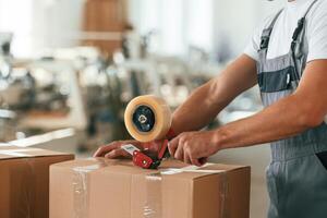 Using, tape, packing the product. Handsome man is working at the factory of creating eco boxes photo