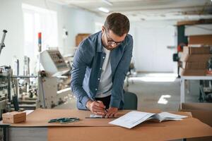 Standing, by the table.. Handsome man is working at the factory of creating eco boxes photo