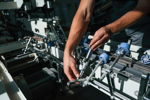 Hands, are adjusting the machine. Handsome man is working at the factory of creating eco boxes photo