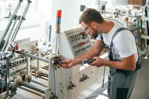 Standing by,, the machine. Handsome man is working at the factory of creating eco boxes photo